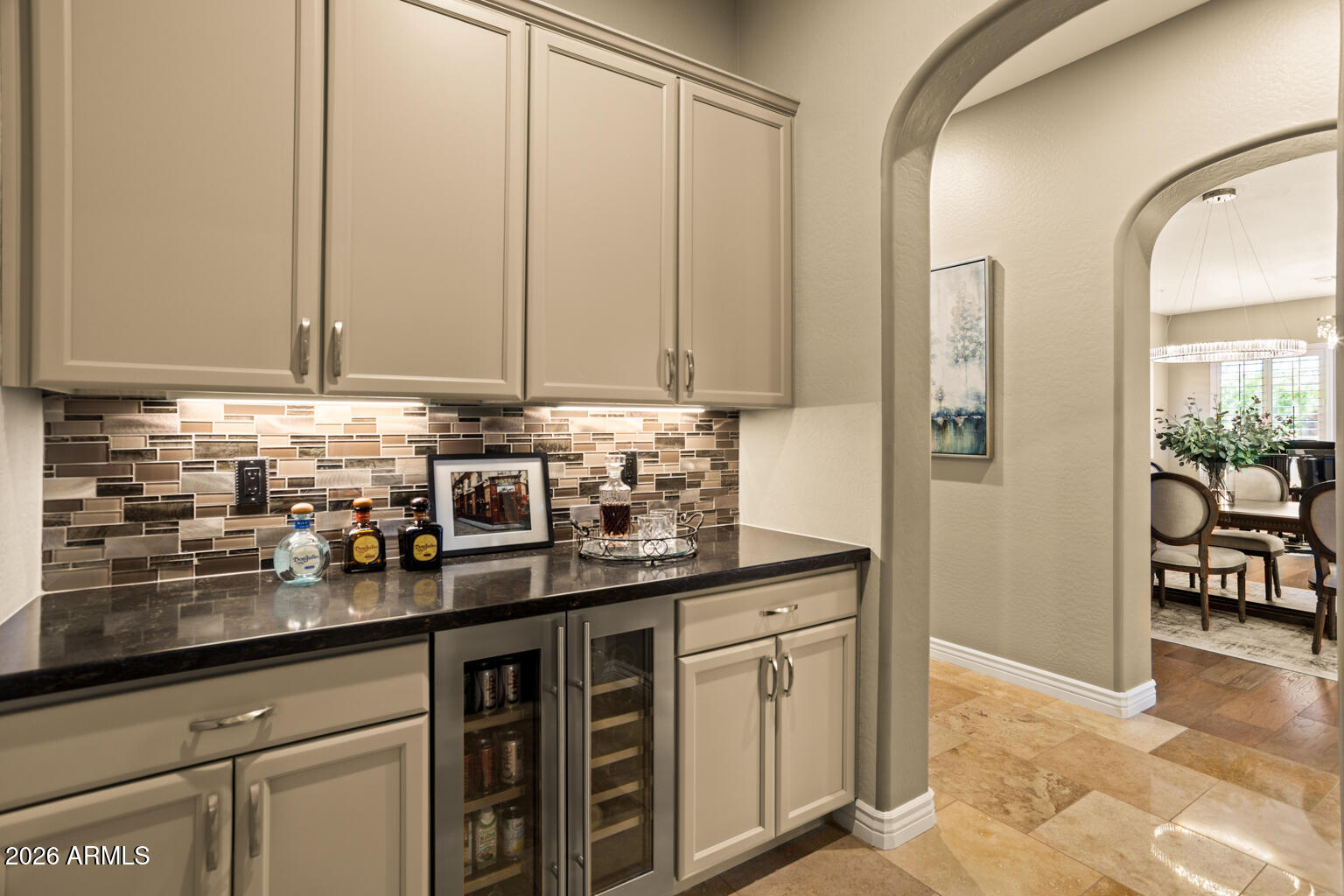 Wet bar with paneled cabinets, mosaic tile backsplash, and arched opening to the dining area.