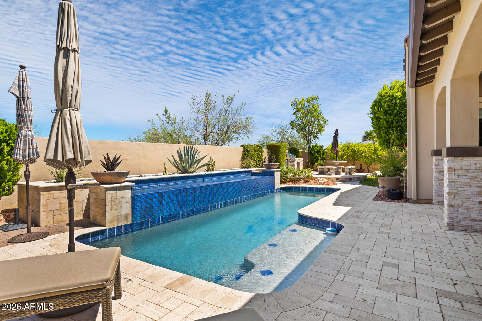Backyard pool with a blue-tiled raised feature, shallow tanning shelf, and stone patio.