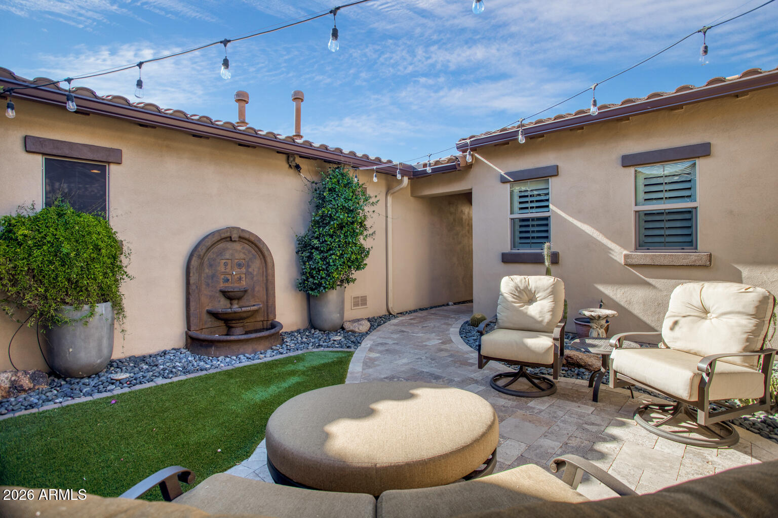 Enclosed courtyard patio with cushioned seating, a stone fountain, string lights, and artificial turf.