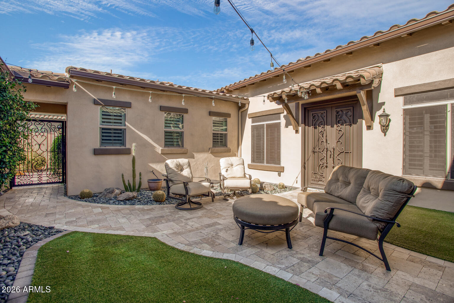Furnished courtyard patio with a curved paver walkway, lawn, desert landscaping, and lounge seating.