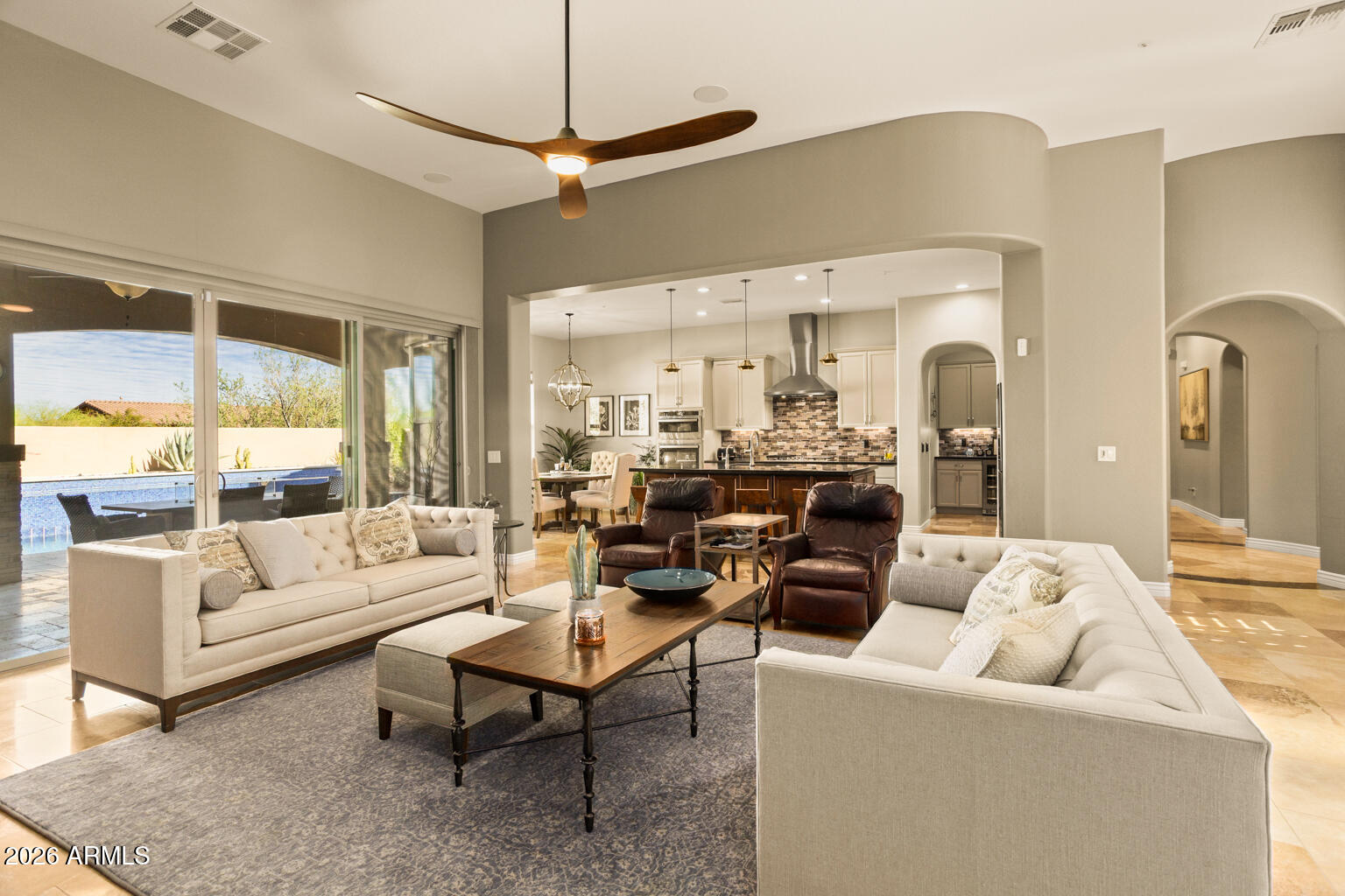 Staged living room with cream sofas, leather armchairs, and sliding doors overlooking a backyard pool.