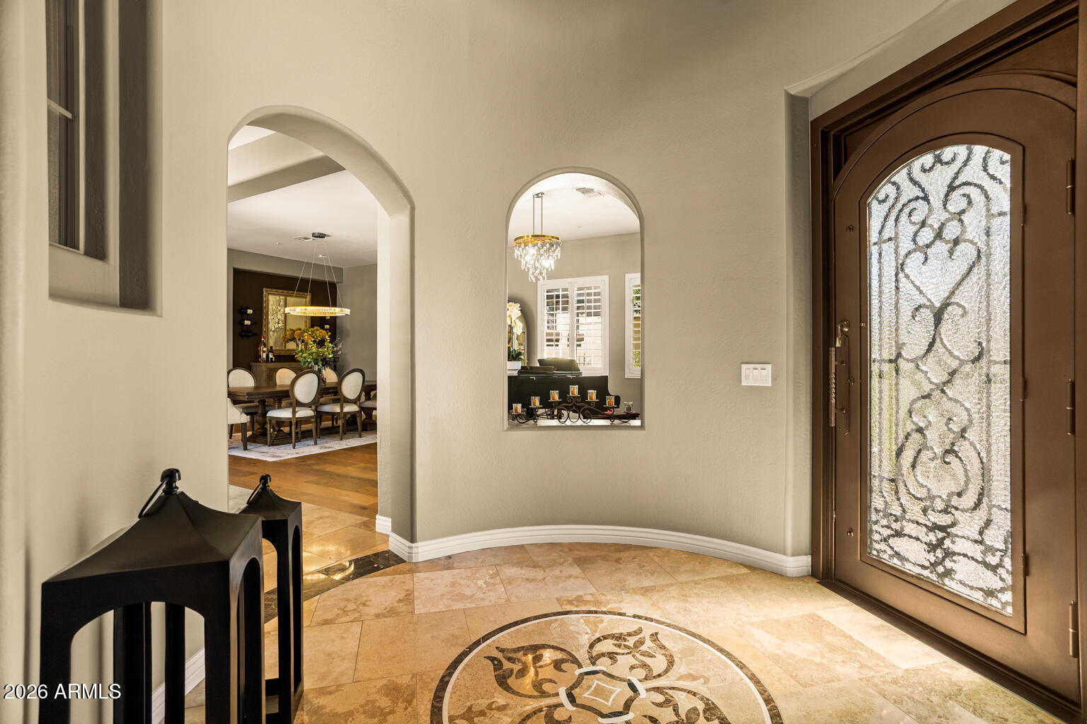 Foyer with a patterned-glass front door, tiled floor medallion, and arched openings to the dining room.