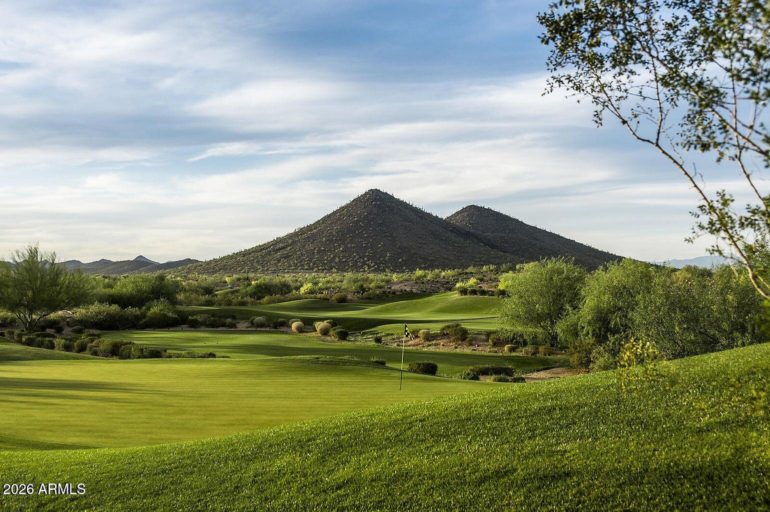 Golf course with a flagstick, rolling fairways, and desert mountains beyond.