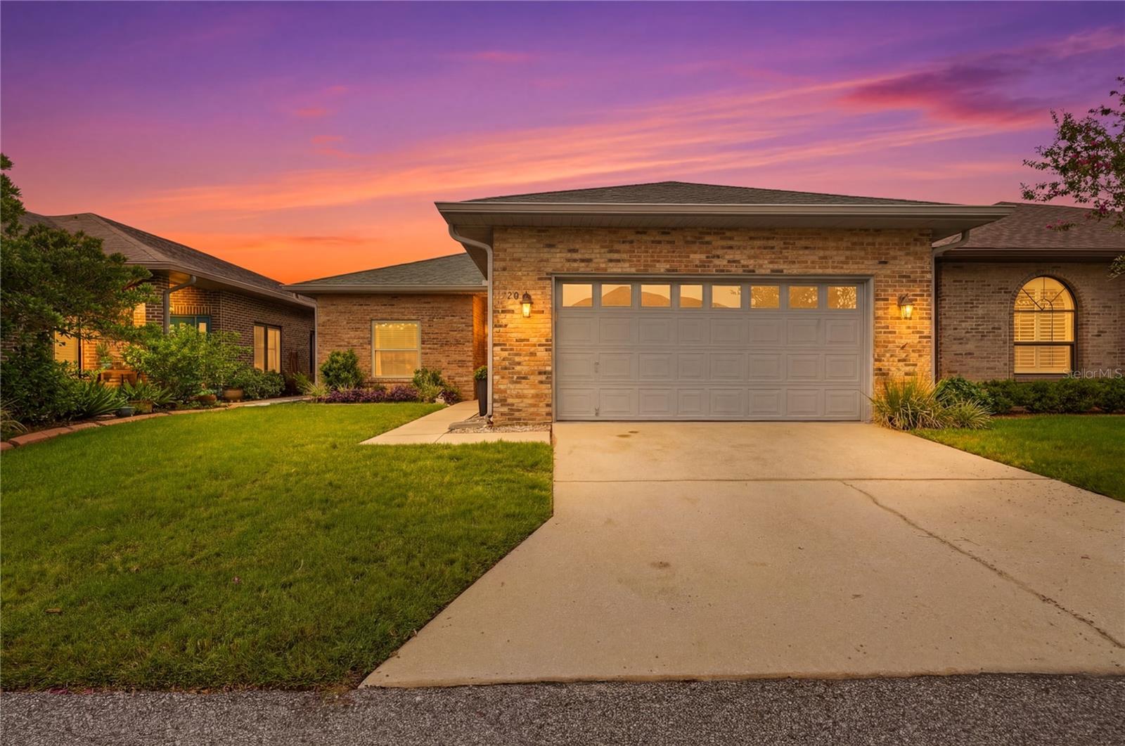 Brick home with a double garage and landscaped lawn at sunset.