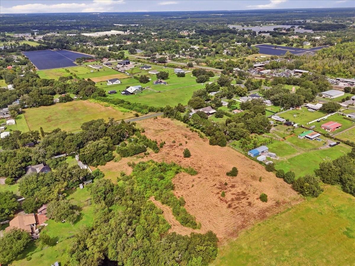 Aerial view of open land with cleared areas, scattered trees, and neighboring properties.