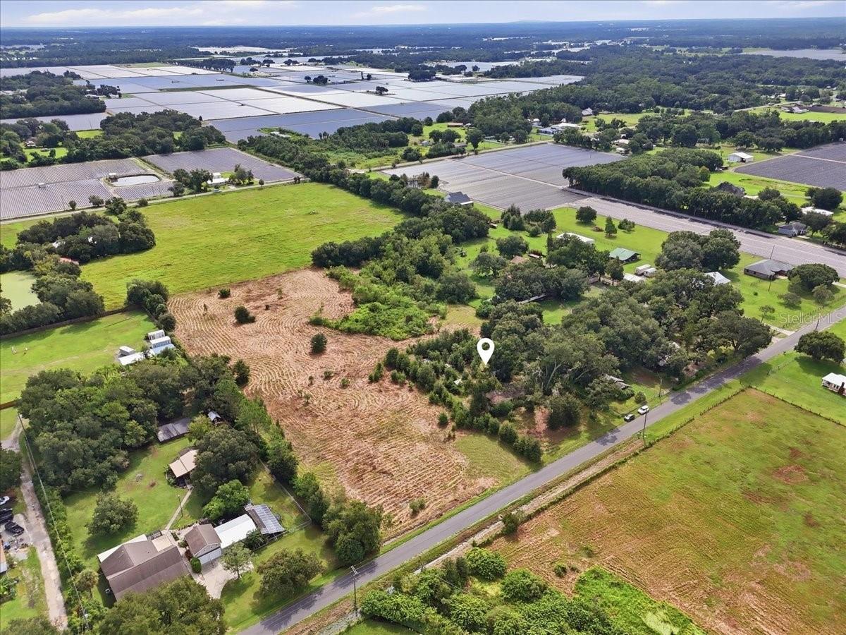 Aerial view of cleared rural acreage among farm fields, homes, and a paved road.