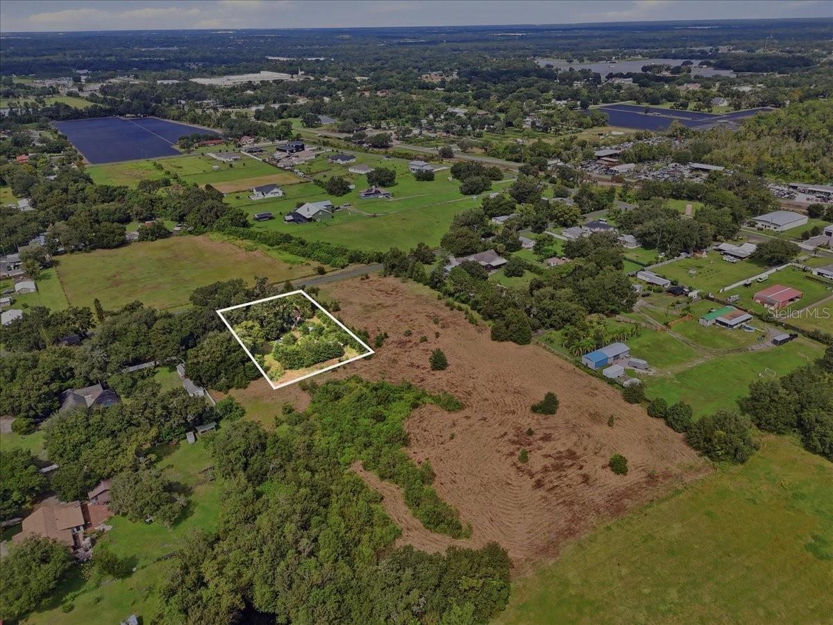 Aerial view of a wooded rural parcel outlined in white, surrounded by fields and scattered homes.