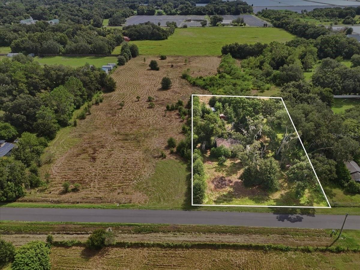 Aerial view of a wooded vacant parcel outlined in white beside a cleared field and road.