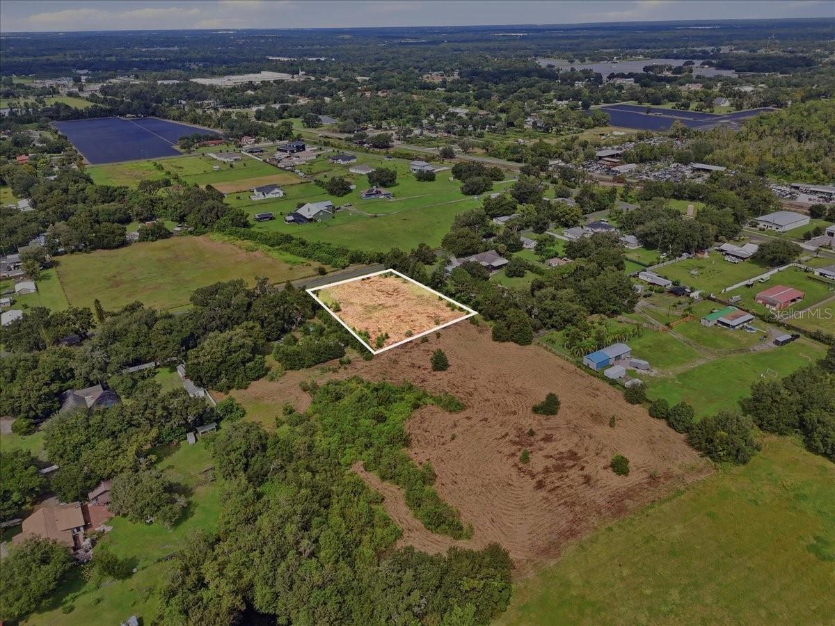 Aerial view of a vacant parcel outlined in white amid fields, trees, and scattered homes.