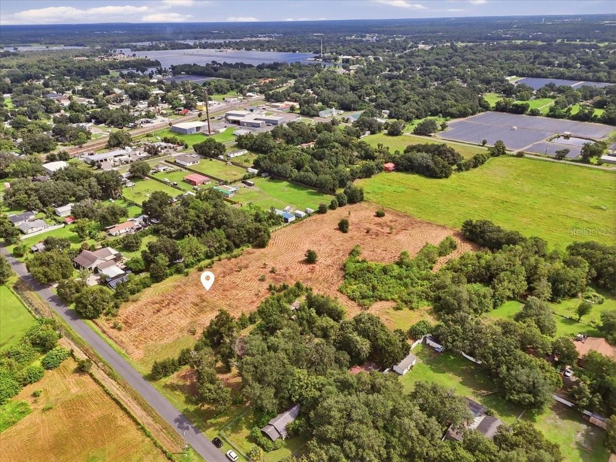 Aerial view of a cleared vacant parcel amid homes, fields, and tree cover.