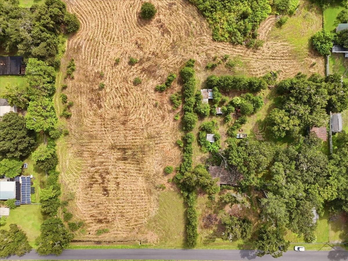Aerial view of a cleared, graded parcel bordered by trees and neighboring homes.
