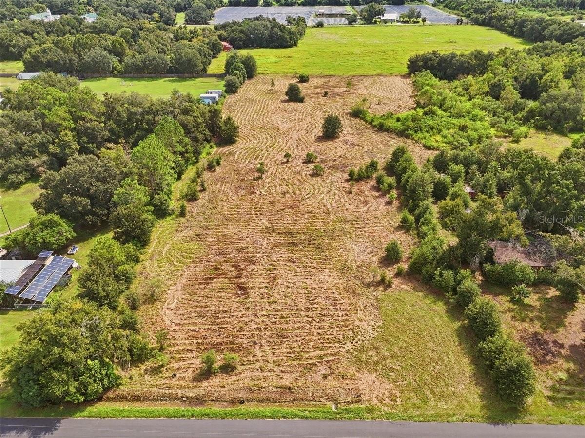 Aerial view of a cleared parcel bordered by trees, with road frontage and surrounding green fields.