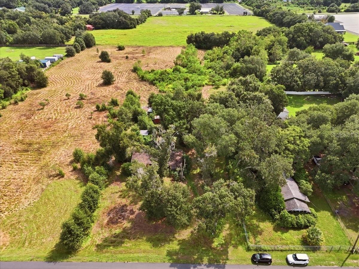 Aerial view of a tree-covered property with a cleared field and a house partly hidden by trees.