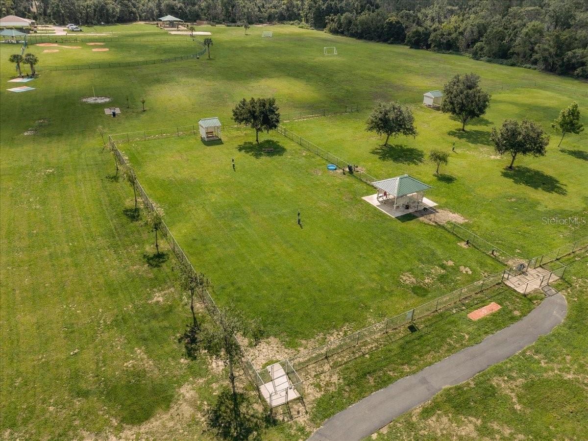 Aerial view of a broad grassy property with fenced sections, scattered trees, and small shelters.