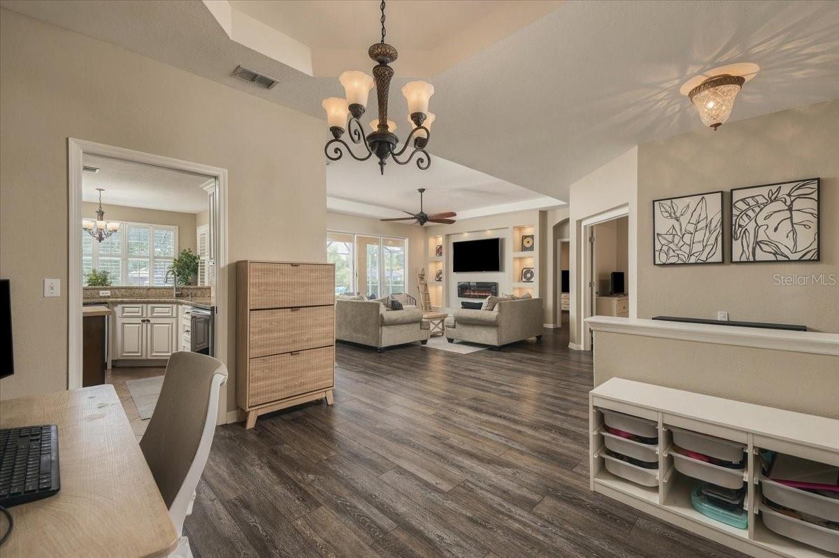 Open-plan living room with light sofas, built-in shelves, large windows, and dark wood-look flooring.