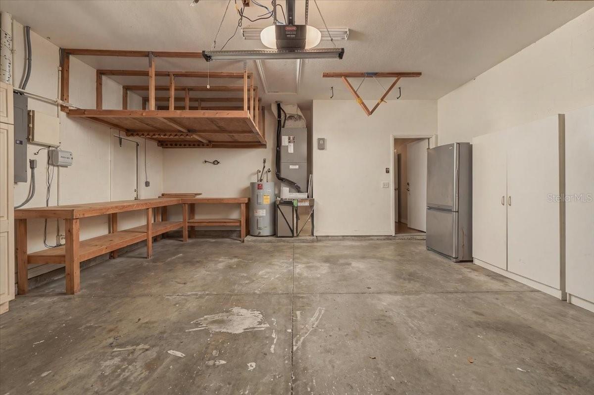 Empty garage with a wooden workbench, overhead storage loft, refrigerator, and built-in cabinets.