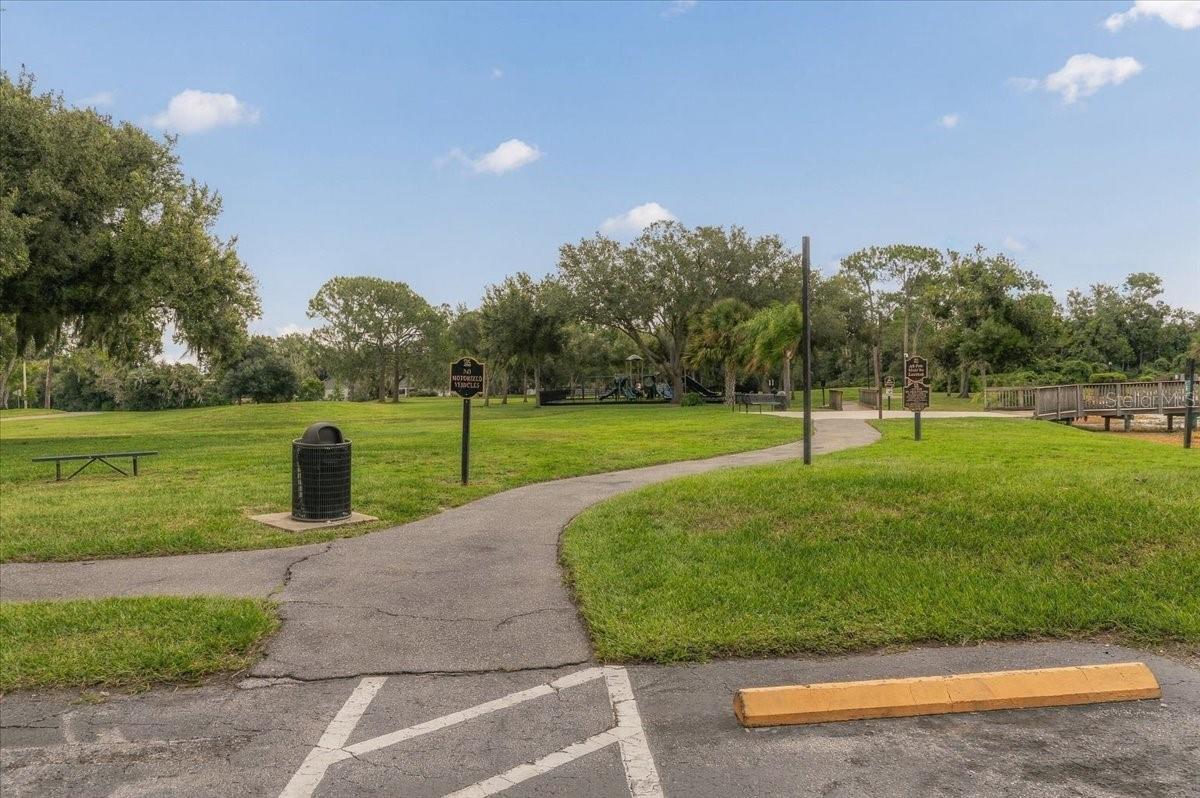 Community park with a winding paved path, grassy lawn, mature trees, and a playground.