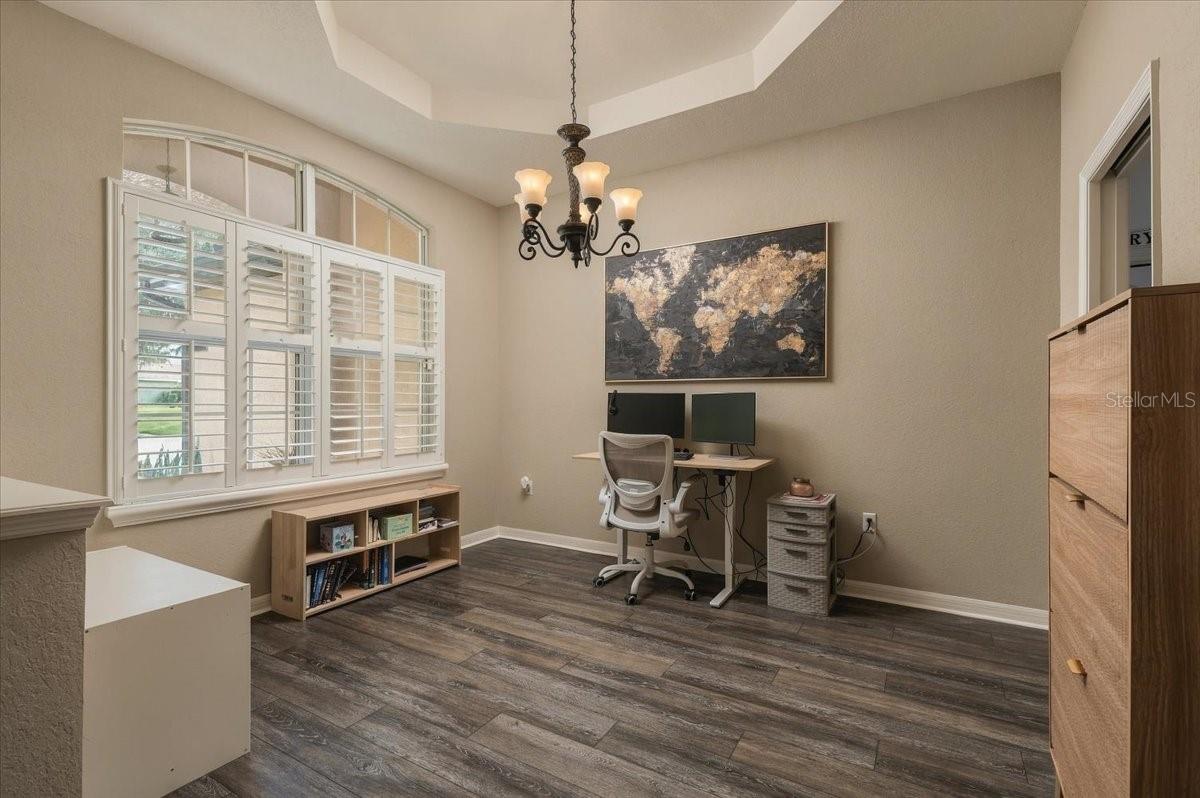 Home office with plantation-shuttered windows, a desk and monitors, and a framed world map.