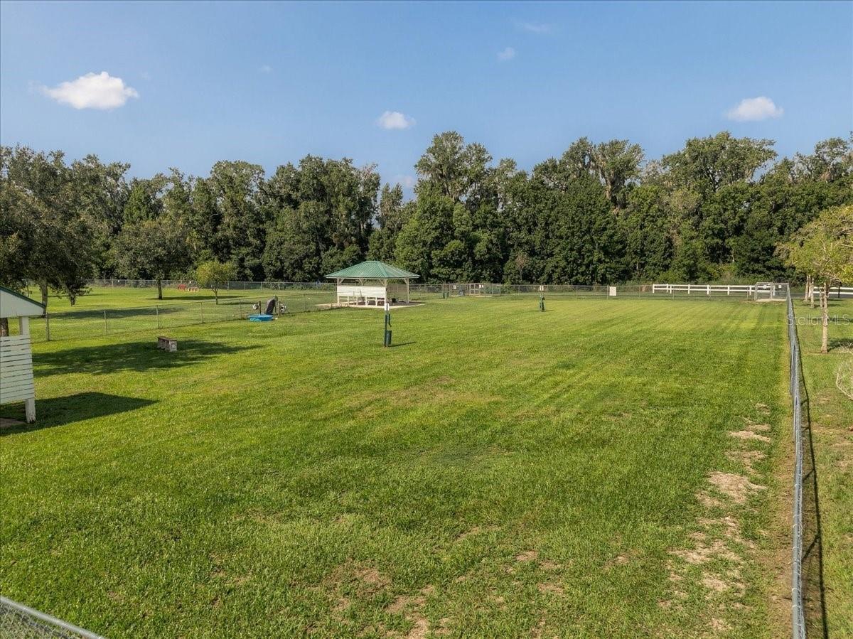 Fenced grassy yard with a green-roofed gazebo and mature trees.