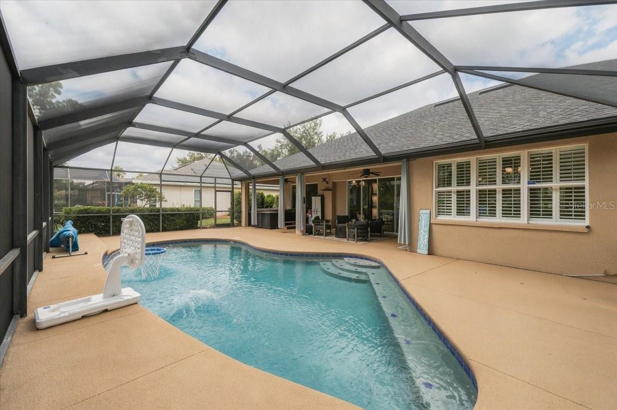 Screened-in backyard pool beside the home's covered patio, with a basketball hoop.