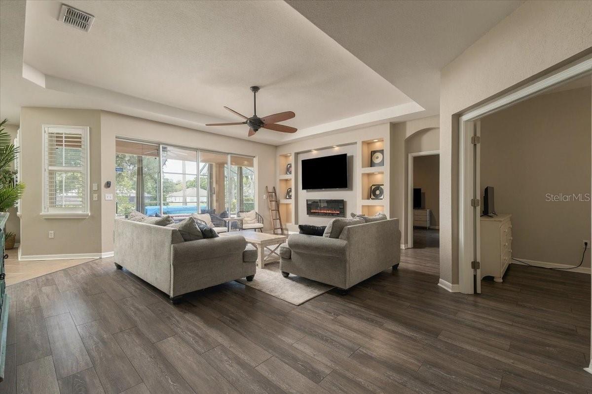 Furnished living room with gray sofas, a fireplace, and sliding glass doors overlooking a pool.