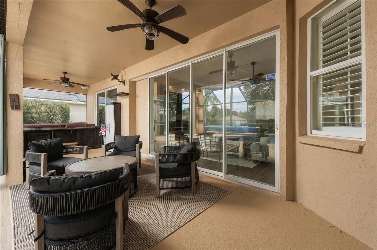 Covered patio with wicker seating, a hot tub, ceiling fans, and sliding glass doors overlooking the pool.