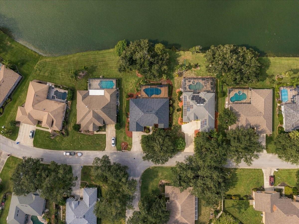 Aerial view of homes and fenced pools along a waterfront street.