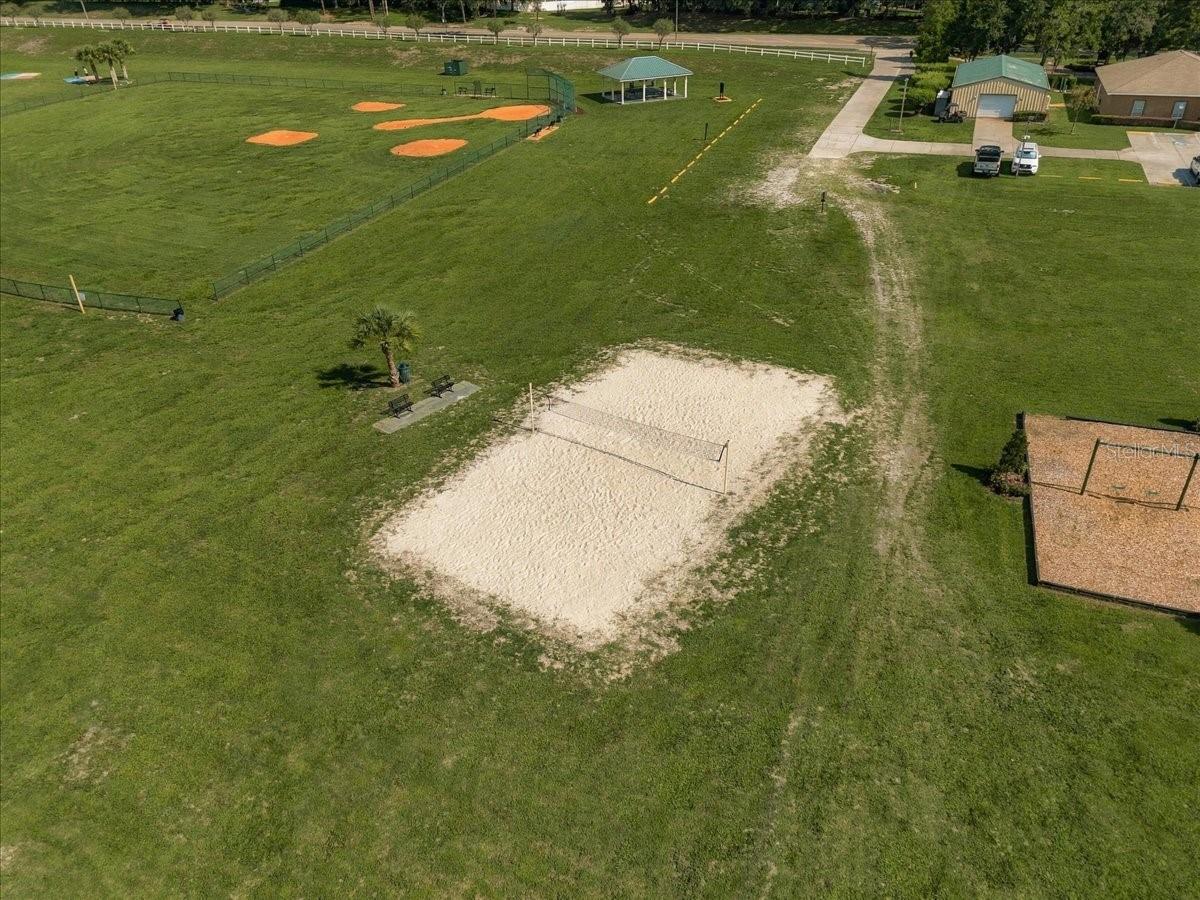 Aerial view of a grassy recreation area with a sand volleyball court and fenced baseball field.