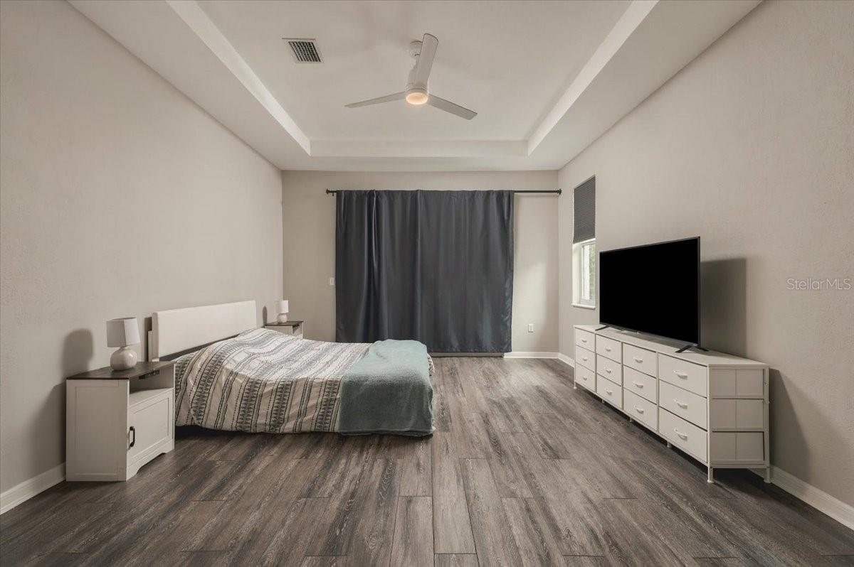 Furnished bedroom with a tray ceiling, dark curtains, and a long dresser topped by a television.