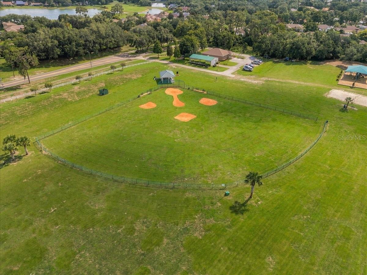 Aerial view of a fenced baseball field with dirt base paths and a covered pavilion.
