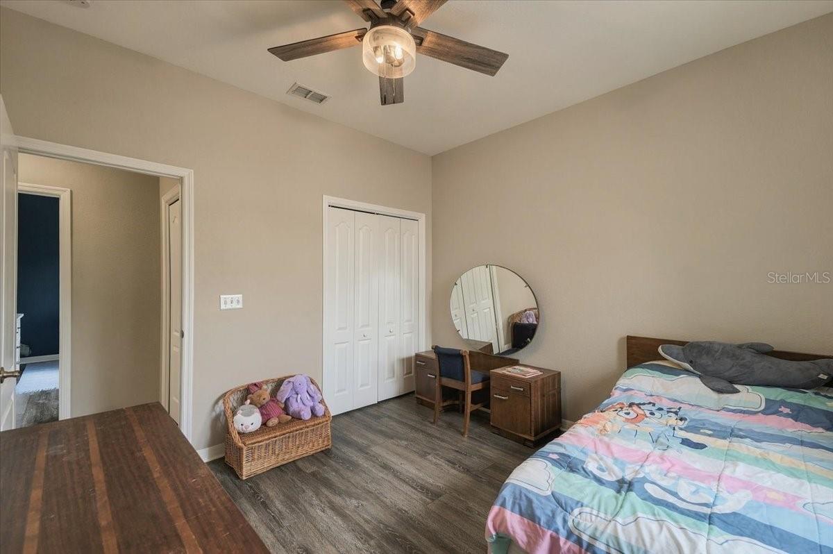 Bedroom with a colorful patterned comforter, wooden vanity, round mirror, and white closet doors.