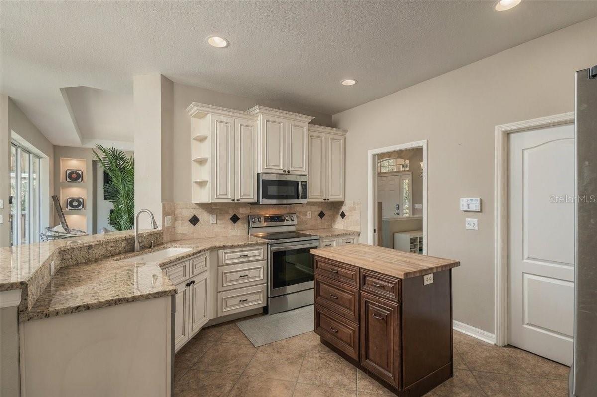 Kitchen with white cabinetry, granite counters, stainless steel appliances, and a dark wood island.