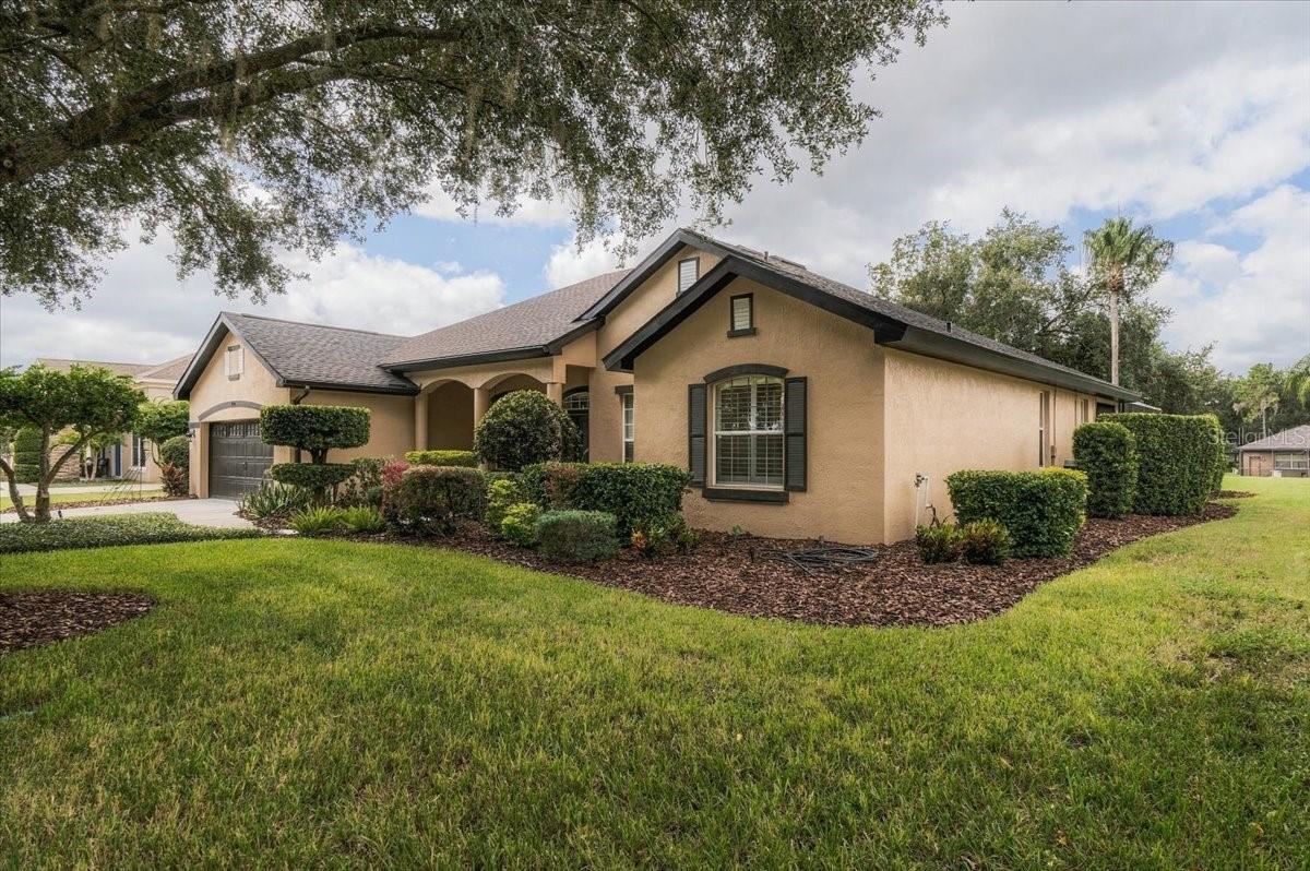 Single-story tan stucco home with an attached garage, landscaped garden beds, and a broad lawn.