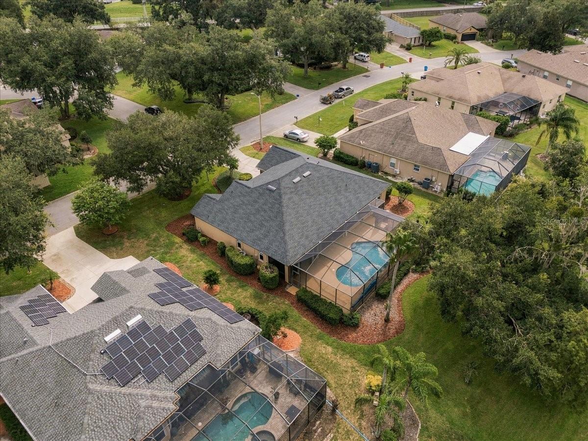 Aerial view of a home with a screened pool enclosure amid a tree-lined residential neighborhood.