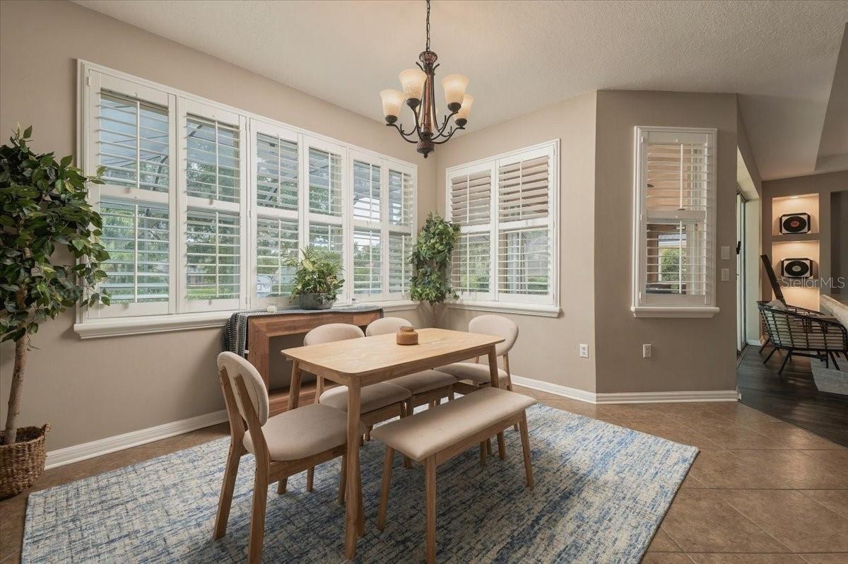 Dining room with plantation-shuttered windows, a wooden table, upholstered chairs, and a chandelier.