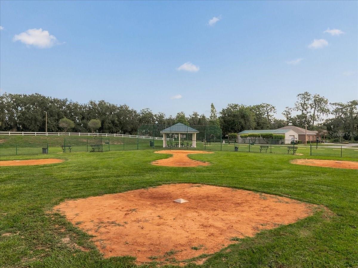 Community baseball field with multiple dirt infields, a fenced backstop, and a covered pavilion.