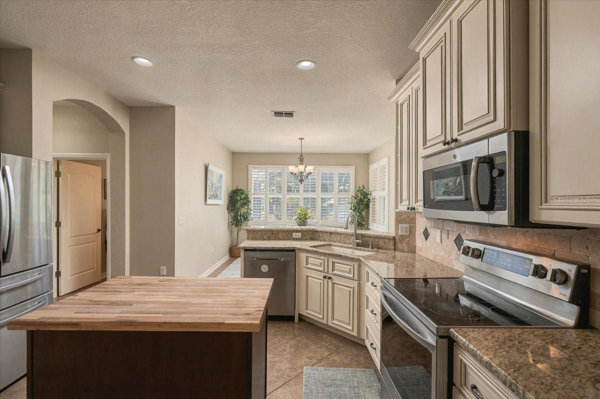 Kitchen with cream cabinets, granite counters, stainless appliances, and a large wood-topped island.
