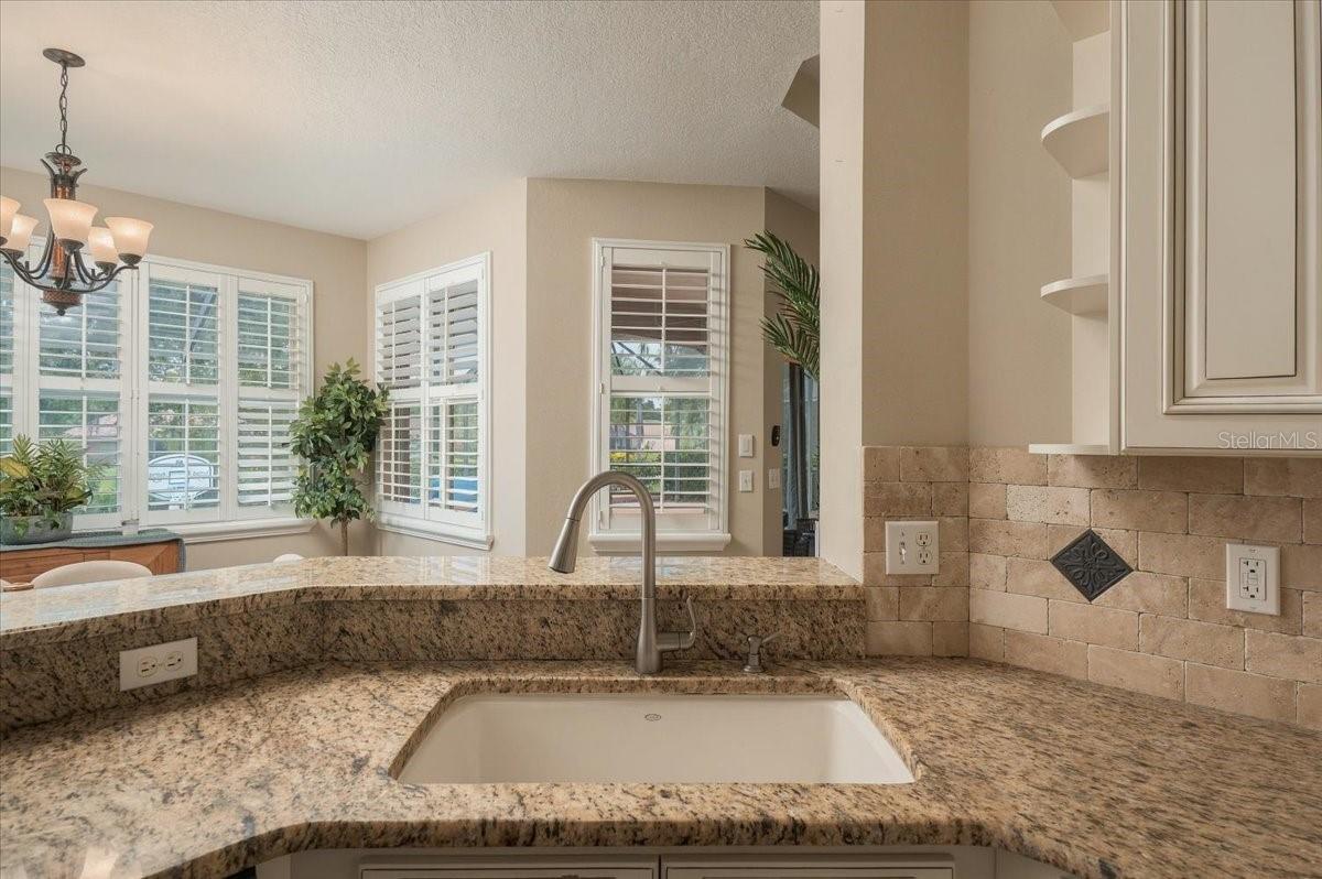 Kitchen with a curved granite counter, inset sink, stone tile backsplash, and shuttered windows.