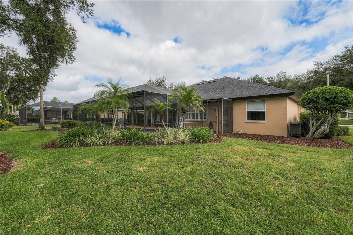Rear of a tan home with a large screened lanai, palm trees, and a broad green lawn.