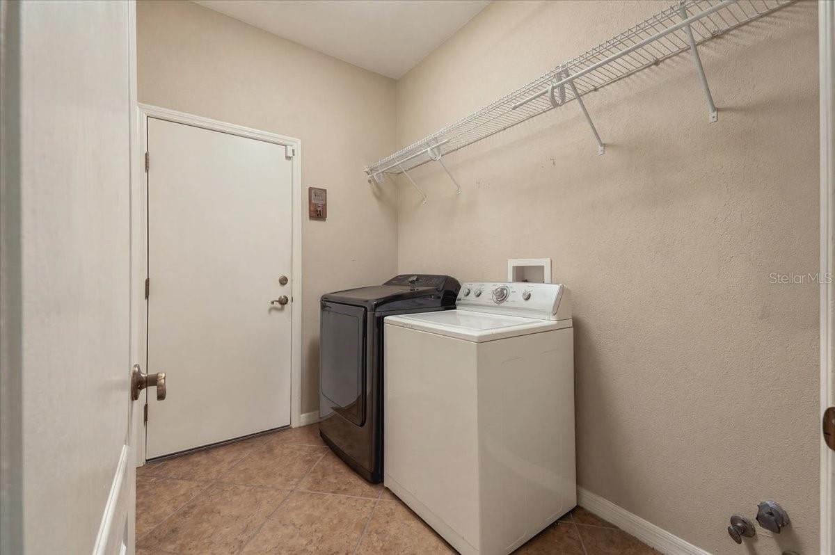 Laundry room with a white top-loading washer, dark front-loading dryer, and overhead wire shelving.