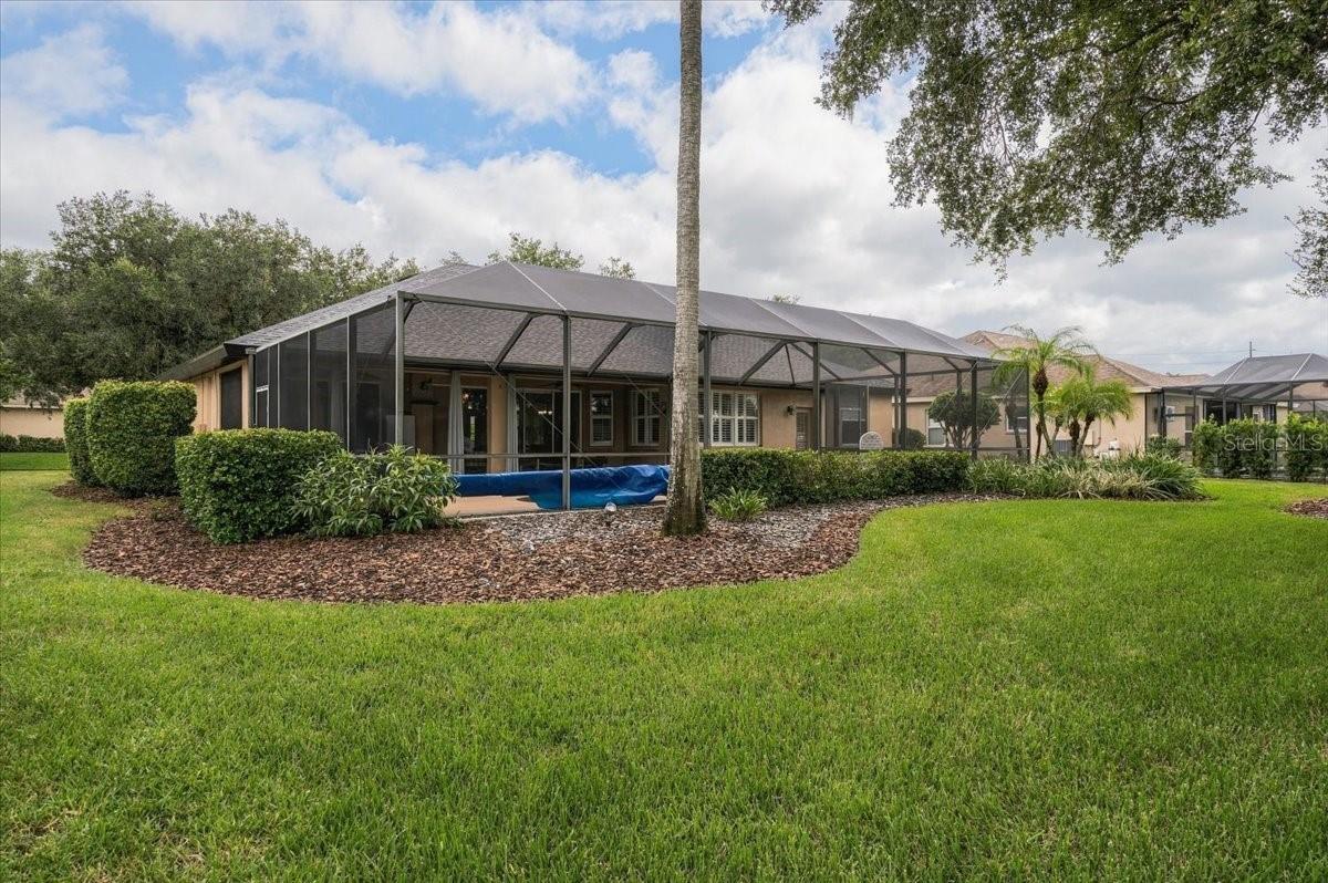 House with a large screened lanai and blue-covered pool opening onto a landscaped lawn.