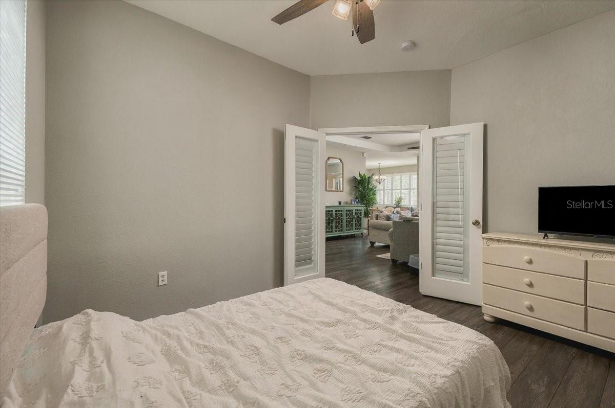 Bedroom with a white quilt and louvered doors opening to a living room.