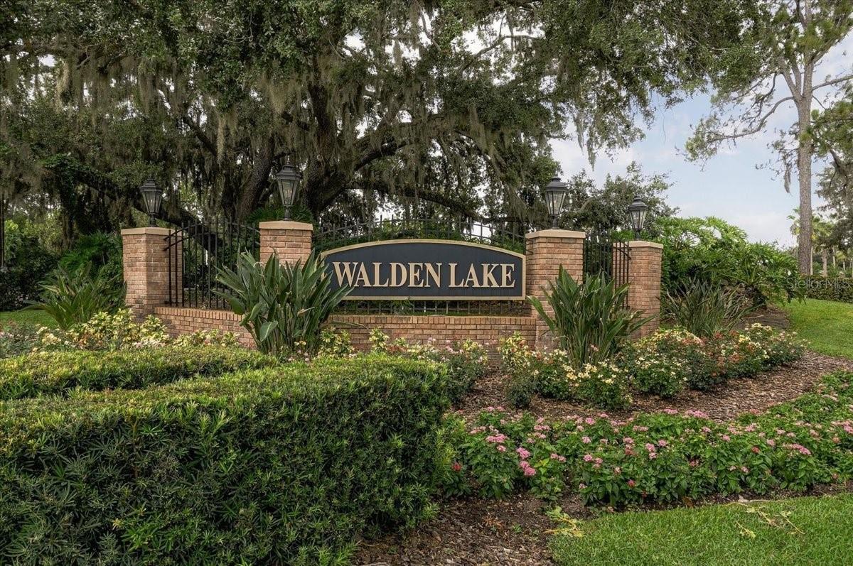 Walden Lake neighborhood entrance sign framed by brick pillars, landscaping, and oak trees.