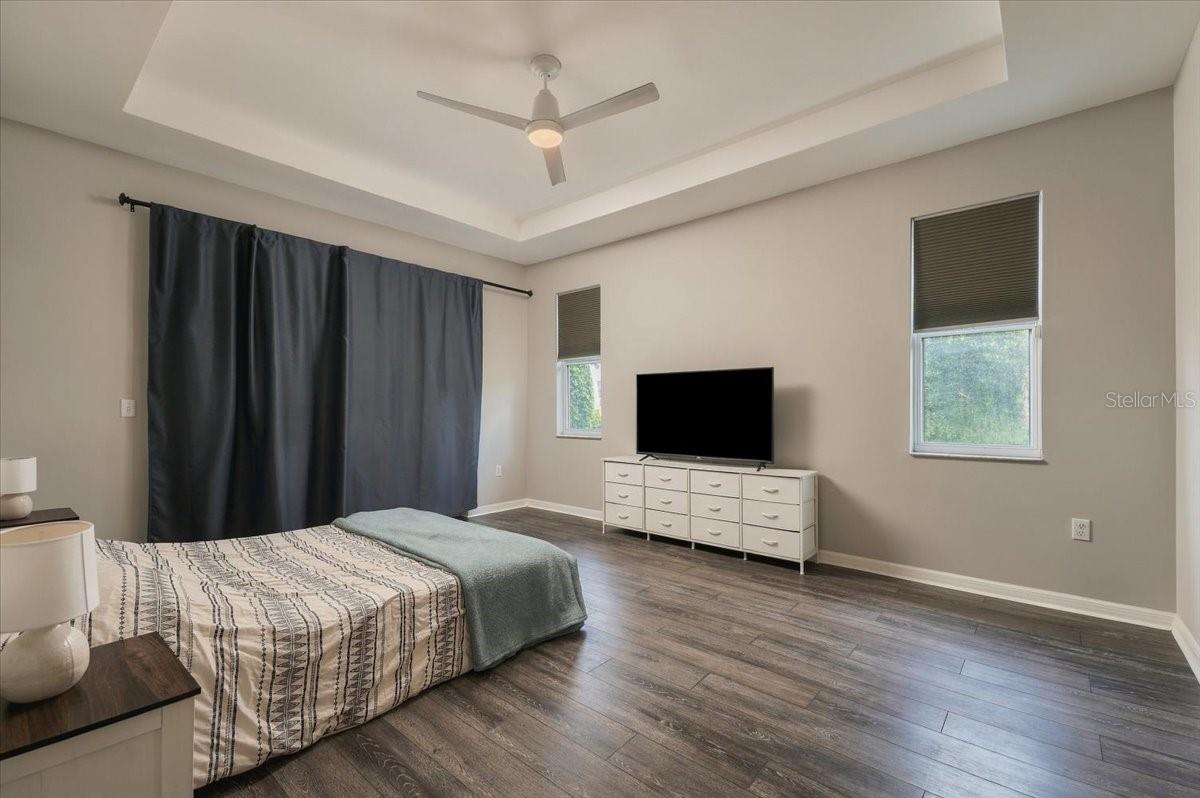 Bedroom with a tray ceiling, dark curtains, and a white dresser beneath a television.