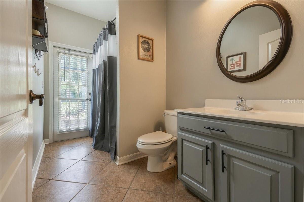 Bathroom with gray vanity and round mirror beside a glass door with blinds and a gray shower curtain.