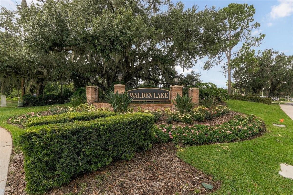 Walden Lake entrance sign among landscaped flower beds and moss-draped oak trees.