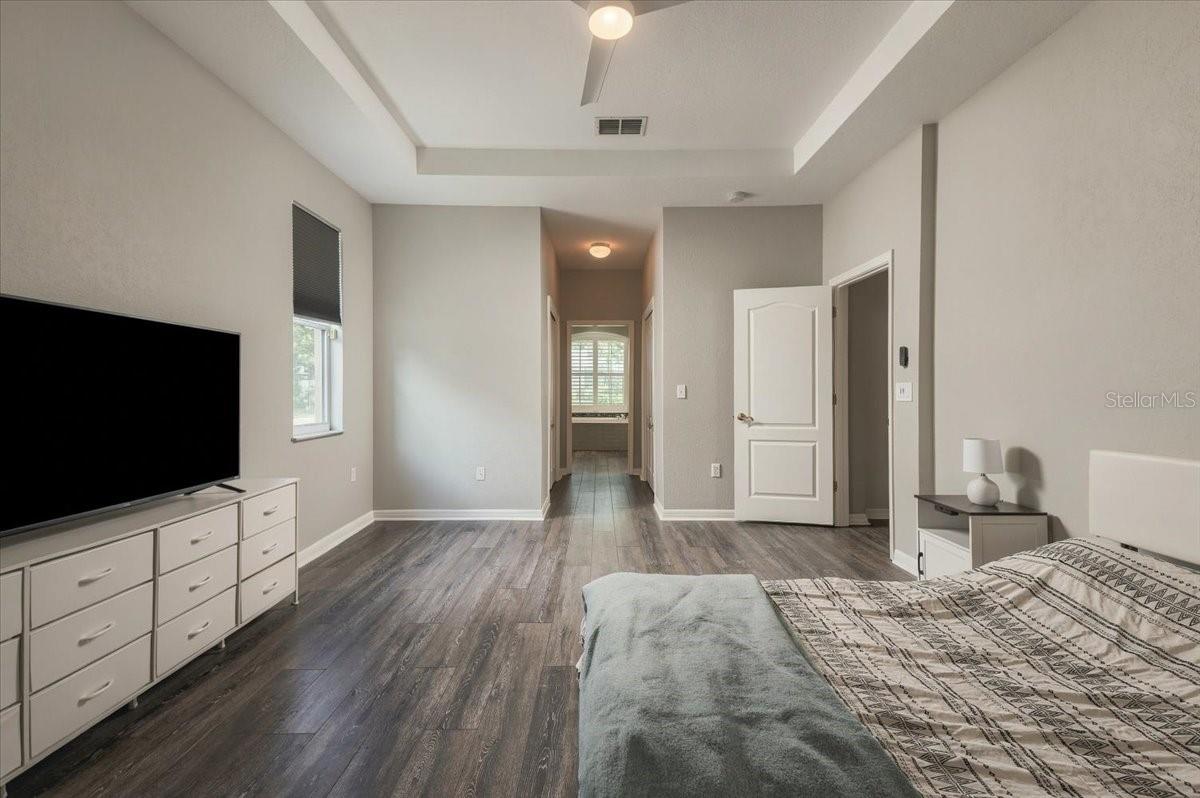 Bedroom with patterned bedding, a television on a white dresser, and a hallway beyond.