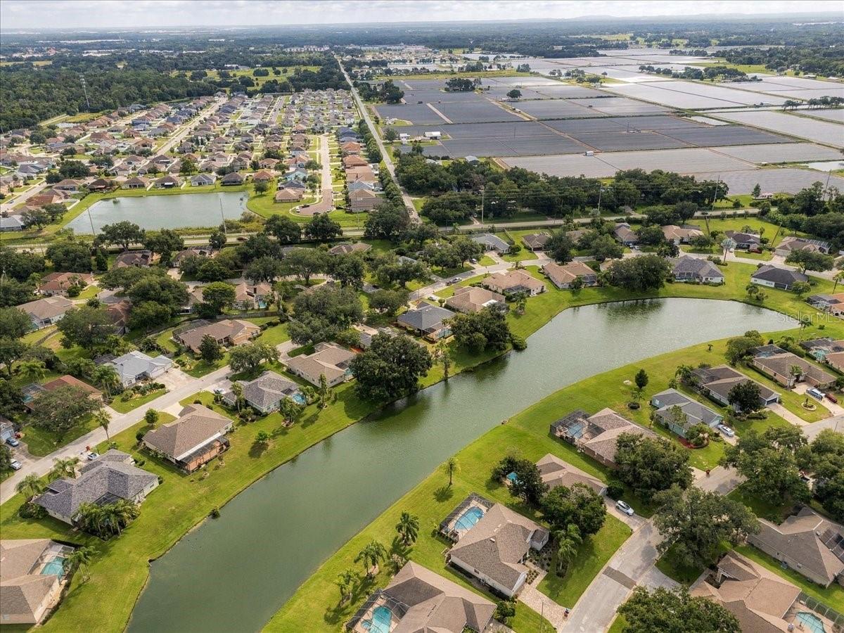 Aerial neighborhood view with homes beside a winding pond and fields in the distance.