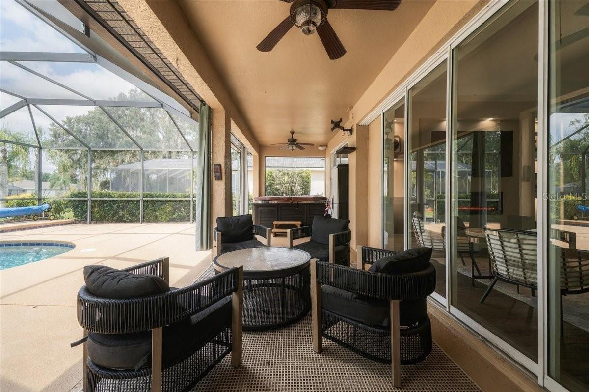 Covered patio with black wicker seating beside a screened pool and hot tub.
