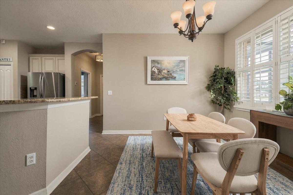 Dining area with a wood table and upholstered chairs beside a kitchen with a granite breakfast bar.